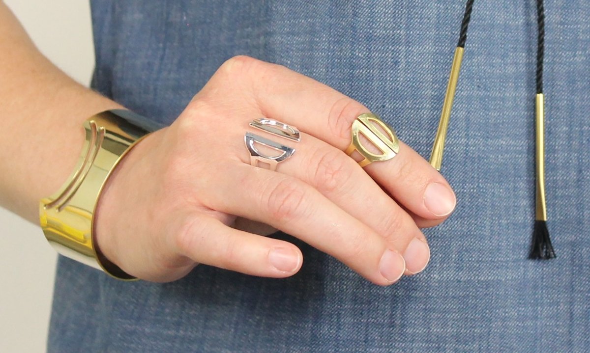 One brass and one silver adjustable Roko ring, worn by a model with a betsy & iya black cotton and brass Tassa necklace, a betsy & iya brass Nisi cuff, and a chambray top.