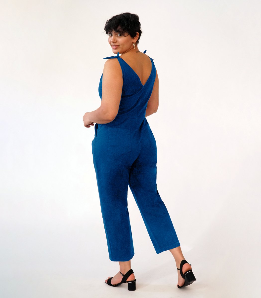 Model shows the back side of a bright blue colored jumpsuit with a V-neckline and tie up shoulder straps. The Slate Overalls in Royal are designed by Loup and made in New York City, USA.