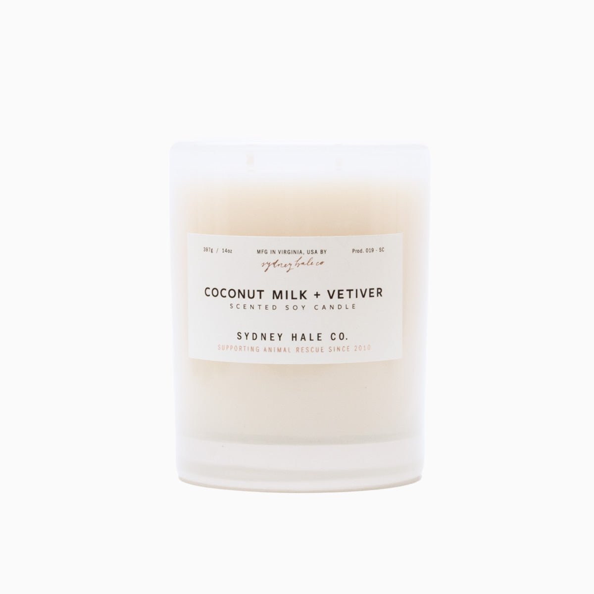 A cylindrical glass candle filled with a soy wax blend and two double cotton wicks. Label reads: "397g/14 oz. Manufactured in Virginia, USA by Sydney Hale Co. Coconut Milk + Vetiver scented soy candle. Sydney Hale Co. Supporting Animal rescue since 2010."