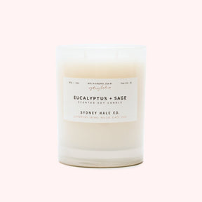 A cylindrical glass candle filled with a soy wax blend and two double cotton wicks. Label reads: "397g/14 oz. Manufactured in Virginia, USA by Sydney Hale Co. Eucalyptus + Sage scented soy candle. Sydney Hale Co. Supporting Animal rescue since 2010."