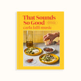 A bright yellow book cover with red and orange font that reads: "THAT SOUNDS SO GOOD. 100 REAL-LIFE RECIPES FOR EVERY DAY OF THE WEEK. CARLA LALLI MUSIC." Cover photo shows two meals with two side accoutrements and a hand grating parmesan over top. That Sounds So Good is by Carla Lalli Music and Published by Penguin Random House.