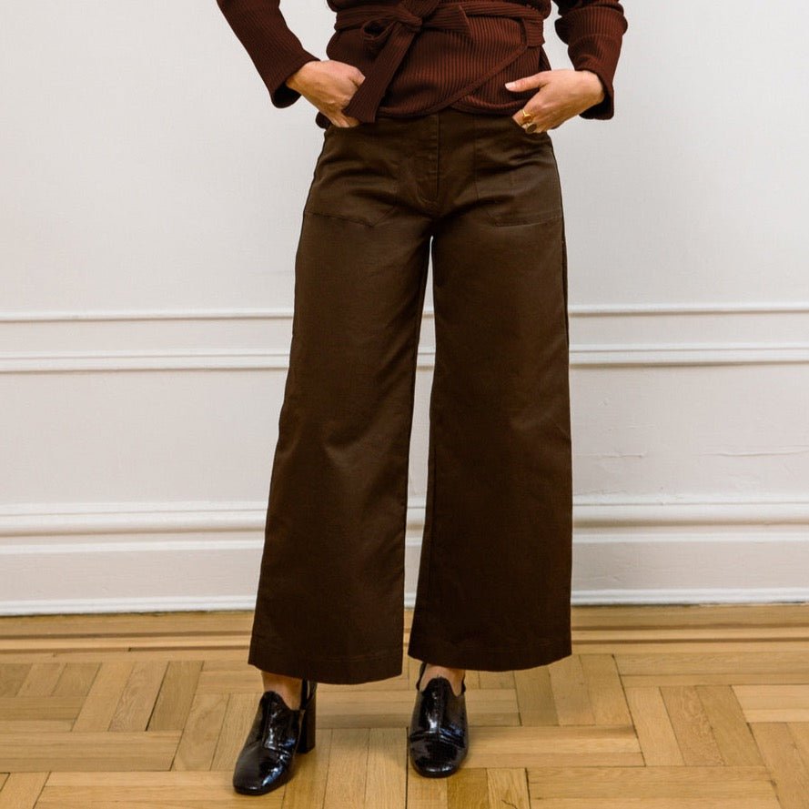 A model wears a high waisted wide leg cropped jean in a dark brown. The Simone Jean in Brown is designed by Loup and made in New York City, USA.
