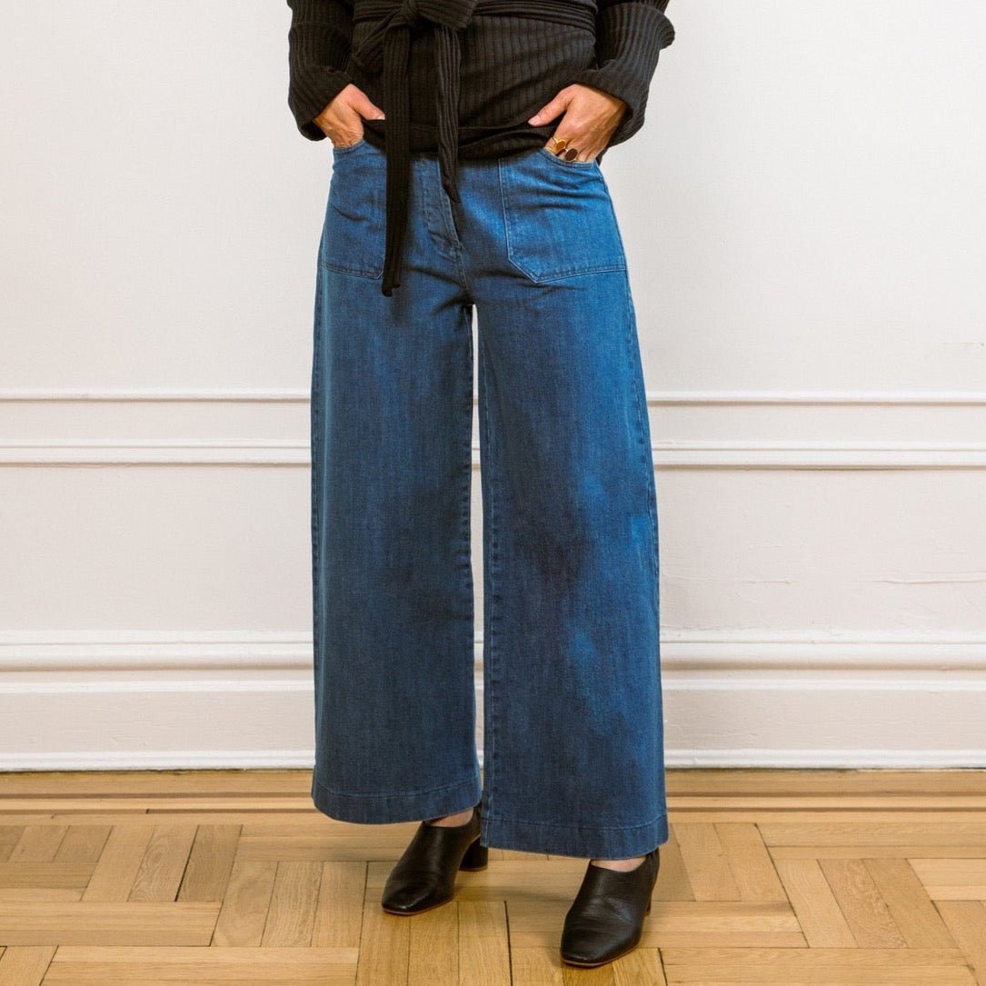 A model wears a high waisted wide leg cropped jean in a blue denim. The Simone Jean in Medium Indigo is designed by Loup and made in New York City, USA.