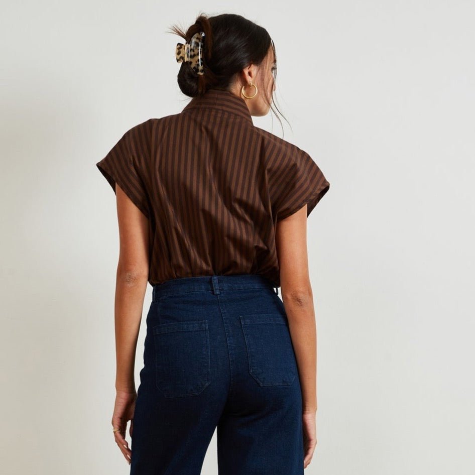 A model shows the backside of a short sleeve tunic button up in brown stripes. Model has shirt tucked into denim jeans. The Sienna Top in brown Stripe is designed by Loup and made in New York City.