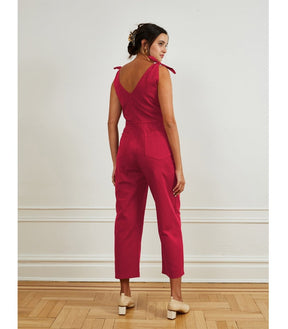 A model shows the backside of a bright pink colored jumpsuit with a V-neckline and tie up shoulder straps. The Slate Overalls in Rose are designed by Loup and made in New York City, USA.