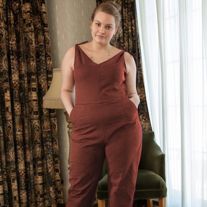 Model wears a rusty red colored jumpsuit with a V-neckline and tie up shoulder straps. The Slate Overalls in Terracotta are designed by Loup and made in New York City, USA.