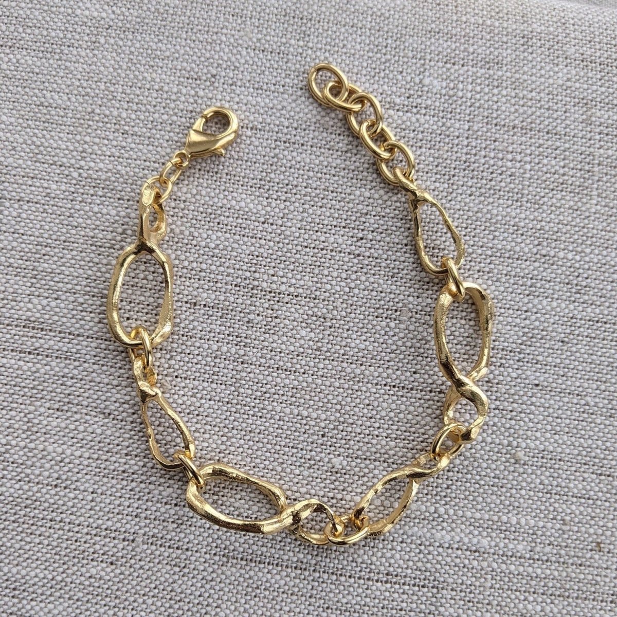 A linked 22 kt gold plated bracelet lays against a gray background. The Small Favors Link Sculptured Bracelet is designed by Lingua Nigra and handcrafted in Chicago, Illinois.