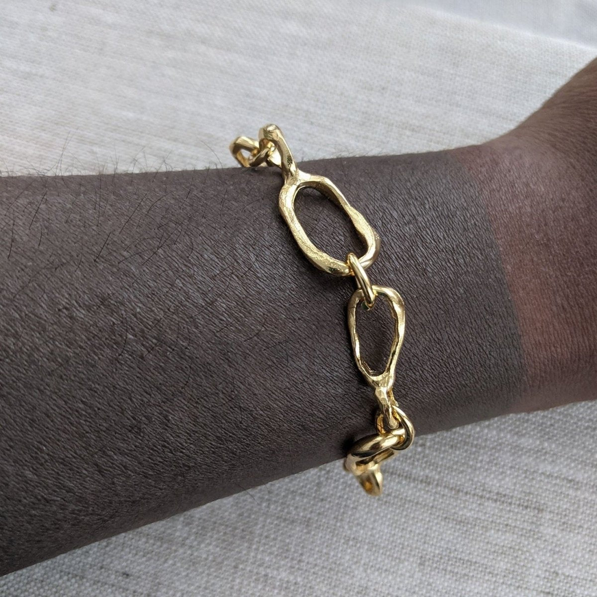 A model wears a linked 22 kt gold plated bracelet around their wrist. The Small Favors Link Sculptured Bracelet is designed by Lingua Nigra and handcrafted in Chicago, Illinois.
