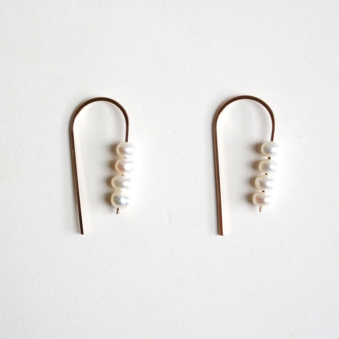A rounded gold tone wire holds four petite freshwater pearls. The Short Arc Threader Earrings are designed and handcrafted by Hooks and Luxe in Jackson Heights, NY.