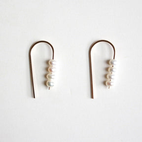 A rounded gold tone wire holds four petite freshwater pearls. The Short Arc Threader Earrings are designed and handcrafted by Hooks and Luxe in Jackson Heights, NY.