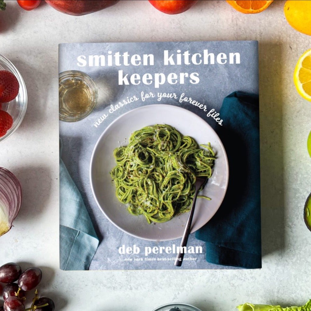 Cover photo shows a bowl of green pasta against a blue background. The white title reads: "SMITTEN KITCHEN KEEPERS: NEW CLASSICS FRO YOUR FOREVER FILES." Authored by Deb Perelman.