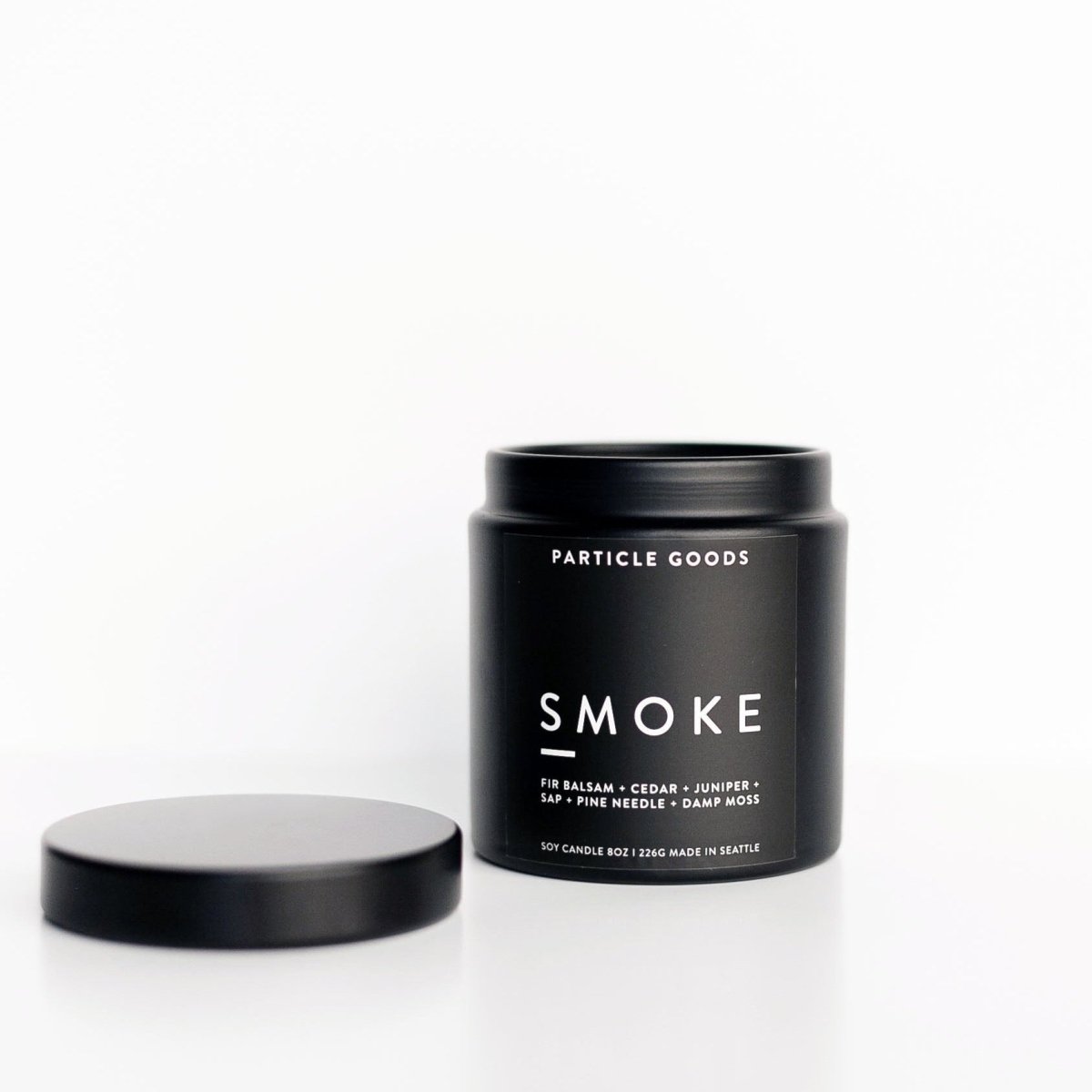 A cylindrical black container holds a soy based wax candle in the scent Smoke. The Smoke candle is hand-poured by Particle Goods in Seattle, WA.