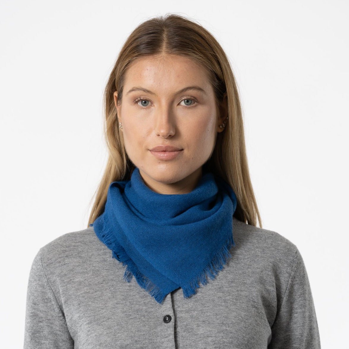 A model wears a square scarf made of 100% Merino wool in a deep blue color. The Merino Square Woven Scarf in Ocean Blue is designed by Dinadi and handcrafted in Nepal.