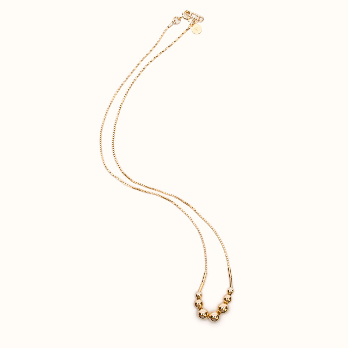 A gold fill necklace featuring a delicate chain and seven round beads flanked by narrow tube beads. The Strella Necklace is designed and handcrafted in Portland, Oregon.