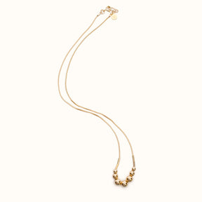 A gold fill necklace featuring a delicate chain and seven round beads flanked by narrow tube beads. The Strella Necklace is designed and handcrafted in Portland, Oregon.
