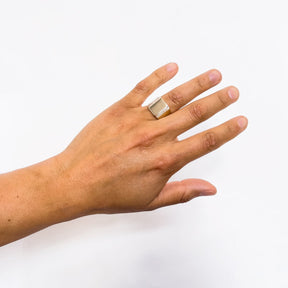 A model wears a wide bang rectangular signet ring with a stair step cut out design. Made of Bronze. The Suscita Ring is designed and handcrafted in Portland, Oregon.