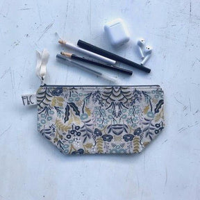 Cosmetic/accessory bag with delicate floral pattern in slate blue, navy, white, blush and metallic gold. Contains a blue zipper with a white twill zipper pull. Designed by Frankie & Coco and handmade in Portland, Oregon.