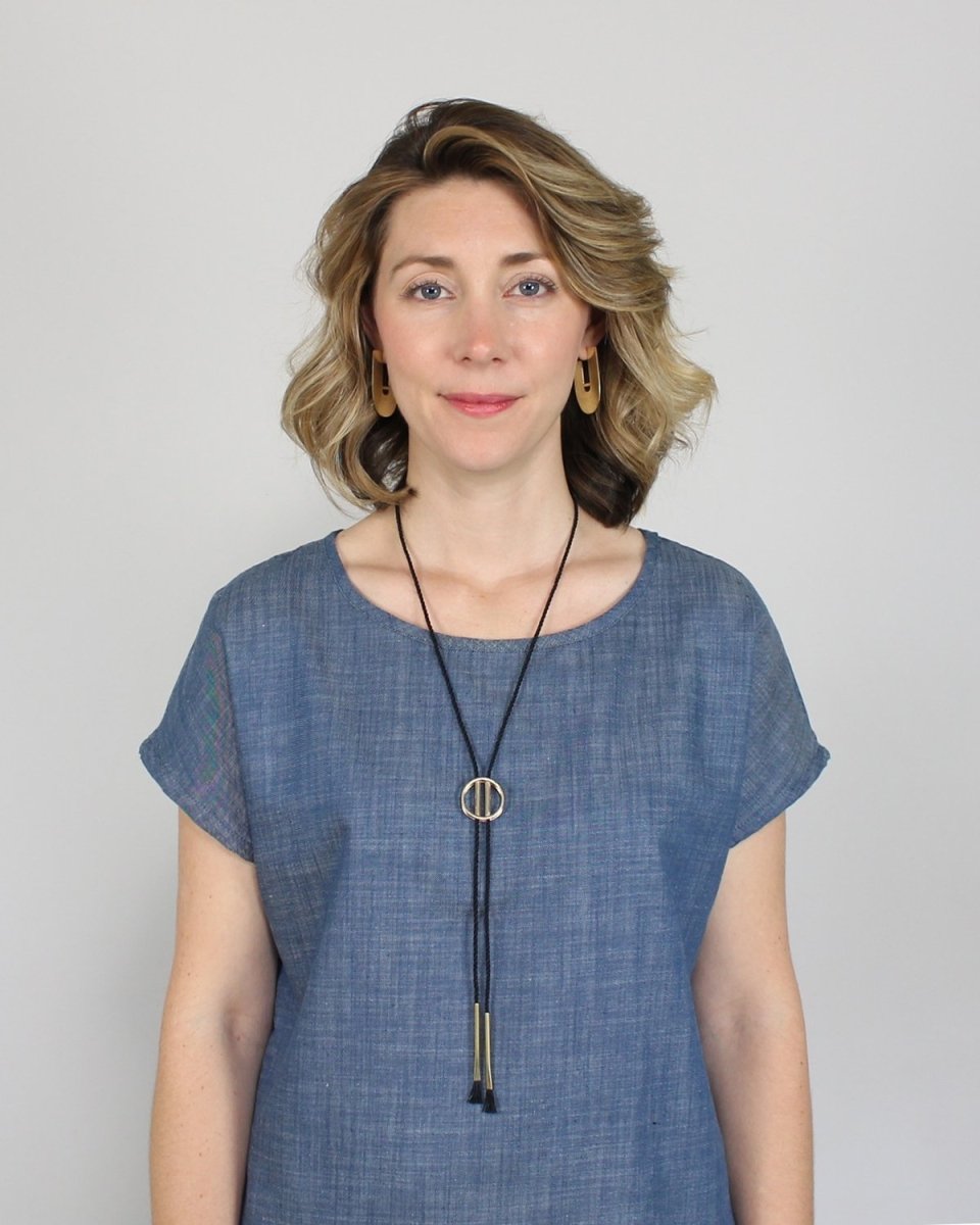 Betsy & iya's black Japanese cotton and brass Tassa bolo necklace, styled on a model with a cap-sleeve denim tunic and (now discontinued) brass betsy & iya Jo hoop earrings.