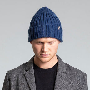 Model wears a dark blue cuffed hat with thick ribbed design and decrease detail at the top. The Merino Thick Rib Hat in Dark Blue is designed by Dinadi and hand knitted in Kathmandu, Nepal.