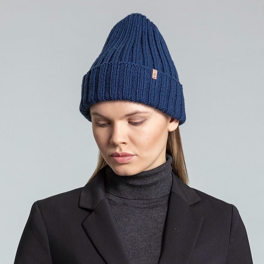 Model wears a dark blue cuffed hat with thick ribbed design and decrease detail at the top. The Merino Thick Rib Hat in Dark Blue is designed by Dinadi and hand knitted in Kathmandu, Nepal.