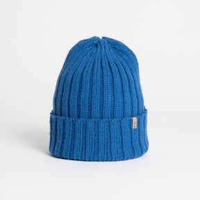 A bright blue cuffed hat with thick ribbed design and decrease detail at the top. The Merino Thick Rib Hat in Ocean Blue is designed by Dinadi and hand knitted in Kathmandu, Nepal.