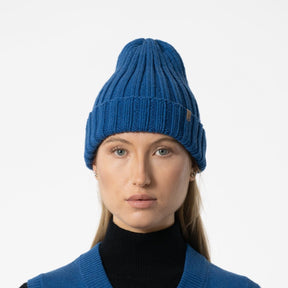 Model wears a bright blue cuffed hat with thick ribbed design and decrease detail at the top. The Merino Thick Rib Hat in Ocean Blue is designed by Dinadi and hand knitted in Kathmandu, Nepal.