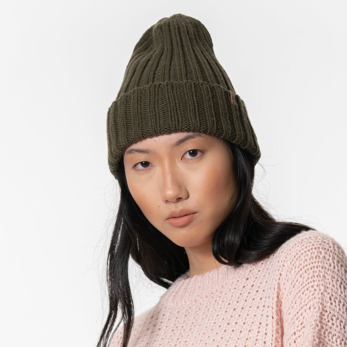 A dark green cuffed hat with thick ribbed design and decrease detail at the top. The Merino Thick Rib Hat in Olive Green is designed by Dinadi and hand knitted in Kathmandu, Nepal.