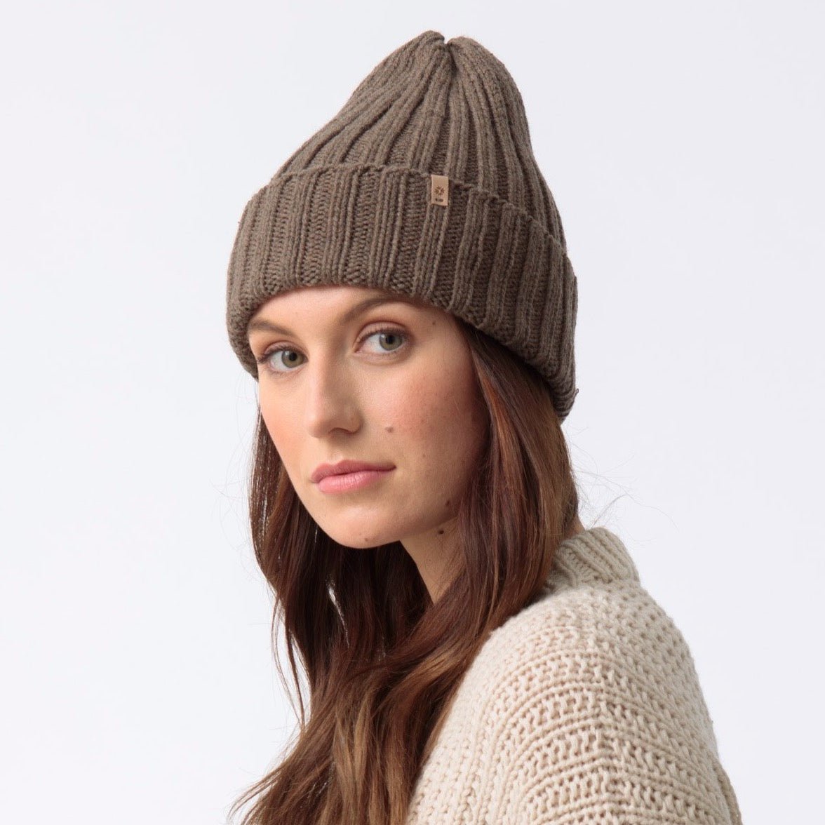 Model wears a dark brown cuffed hat with thick ribbed design and decrease detail at the top. The Merino Thick Rib Hat in Nutmeg Brown is designed by Dinadi and hand knitted in Kathmandu, Nepal.