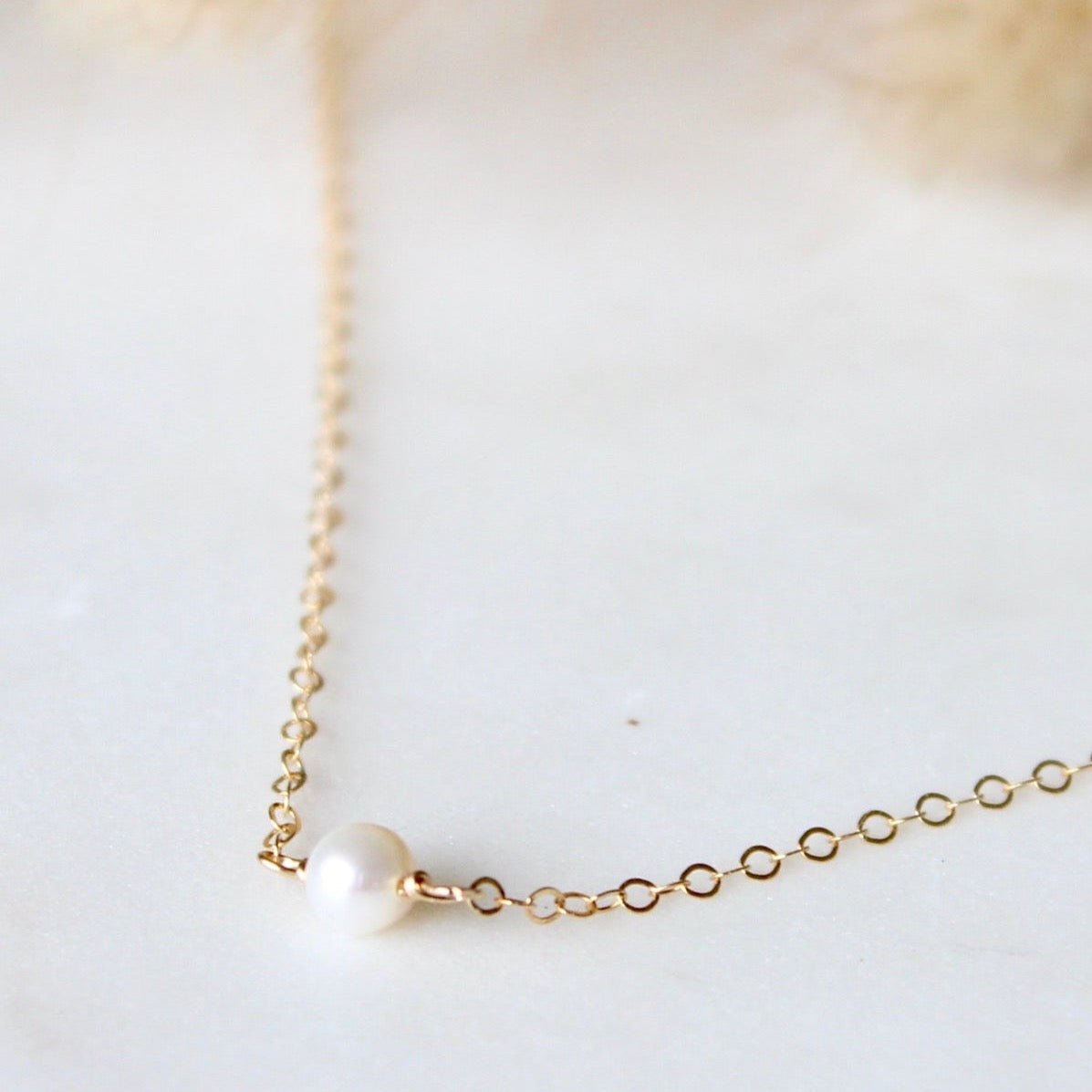 A dainty chain necklace with a tiny freshwater pearl focal piece. The Tiny Freshwater Pearl Necklace is handcrafted by Hello Adorn in Eau Claire, WI.