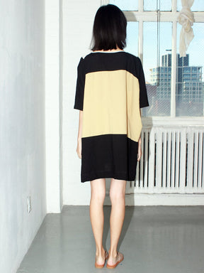 Model shows back side of Red, blue, black, white and pale yellow colored tunic style dress with color-blocked triangle design. Designed and sewn by Uzi in Brooklyn, New York.
