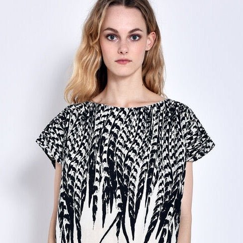 A model wears a short sleeve white top with a black feather design. The Tunic in Cream feather is designed and sewn by Uzi NYC in Brooklyn, New York.