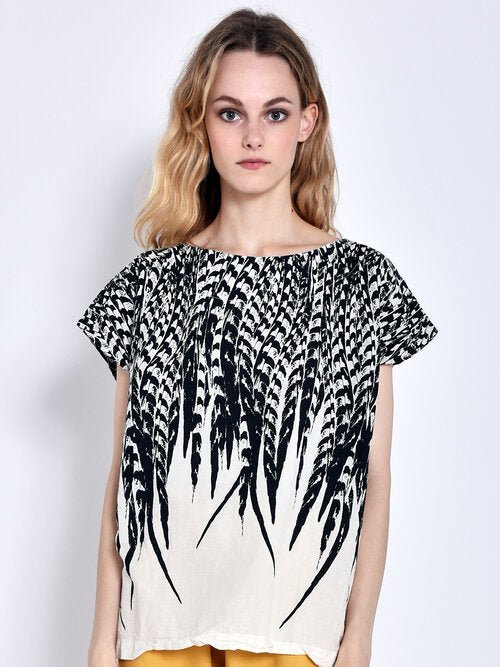 A model wears a short sleeve white top with a black feather design. The Tunic in Cream feather is designed and sewn by Uzi NYC in Brooklyn, New York.