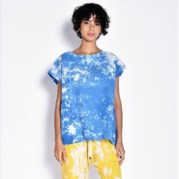 A model wears a bright blue and white tie dye designed short sleeve top. The Tunic in Sky Dye is designed and sewn by UZI NYC in Brooklyn, New York.