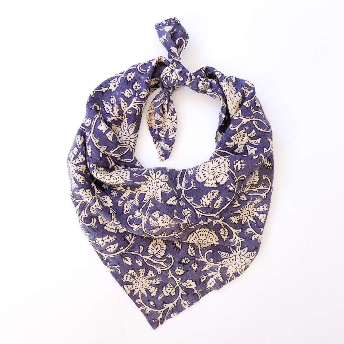 A violet and cream floral patterned bandana, folded over and tied in a knot. Block printed by hand, the Alma Bandana from Maelu is designed in Portland, Oregon and handmade in India.