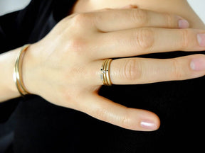 A stack of 14k yellow gold and diamond Vis, Manus, and Robur betsy & iya rings, pictured on a model with a black shirt and two betsy & iya gold Mollia Cuff bracelets.