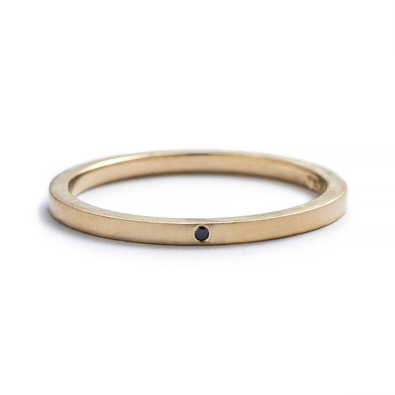 Thin, 14k yellow gold stacking band with a matte finish, and a tiny, round, flush-set black diamond. Hand-crafted in Portland, Oregon. 
