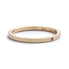 Thin, 14k yellow gold stacking band with a matte finish, a tiny, round, flush-set black diamond, and the betsy & iya logo engraved on the inner band. Hand-crafted in Portland, Oregon. 