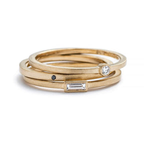 A stack of three 14k yellow gold betsy & iya rings: Robur Ring with a round, bezel-set white diamond, Vis Ring with a round, flush-set black diamond, and Nitor Ring with a white diamond baguette. Hand-crafted in Portland, Oregon.