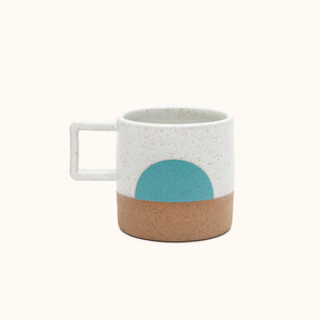 A mug with a white speckled and natural clay finish with a half moon design in a bright teal. The Speckled Moonrise Mug is designed and handmade by Wolf Ceramics in Portland, Oregon.