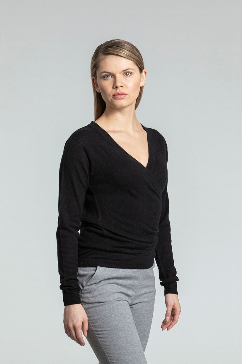A model wears a black knitted wrap cardigan with wraps tied behind the back for a fitted look. The Merino Wrap Cardigan in Black is designed by Dinadi and made in Kathmandu, Nepal.