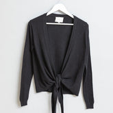 Black knitted wrap cardigan displayed on a white hanger. The Merino Wrap Cardigan in Black is designed by Dinadi and made in Kathmandu, Nepal.