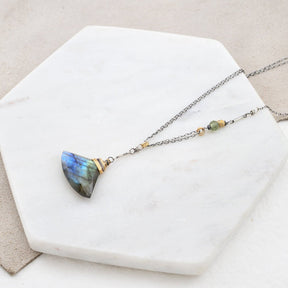 A labradorite necklace lays on a marble slab. The Luna Necklace features a green garnet bead and brass nugget on the sterling chain. Made in Portland, Oregon by designer Amy Olson.