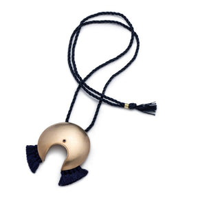 Large, circular, cast-bronze focal piece, featuring a u-shaped cutout at the bottom of the circle, a blue, bezel-set, lapis lazuli stone, and navy blue cotton fringe, threaded with an adjustable, navy blue cotton cord. Hand-crafted in Portland, Oregon. 