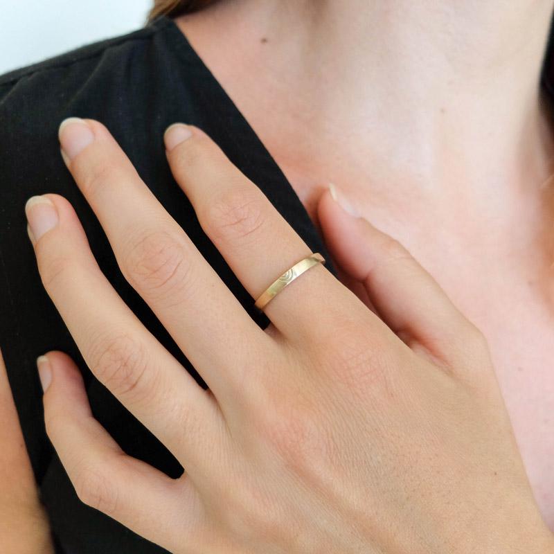 Thin, flat, 14k yellow gold Amandi band with a matte finish, worn on a model's index finger.