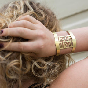 The brass Steel Bridge cuff bracelet by betsy & iya, pictured on the wrist of a model with curly, blonde hair.
