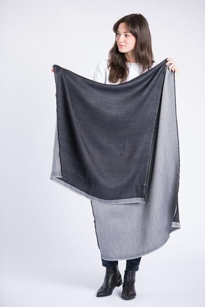 Woman holds out Eden Reversible scarf to show its size. The Eden Reversible Scarf in Black is from Bloom & Give.