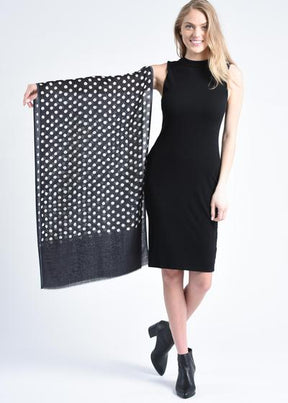 Blonde woman posing has an arm outstretched with a scarf draped along her arm. The scarf is black with white dots. The Maya Dot Scarf in Black is from Bloom & Give.