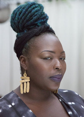 A woman models big brass earrings with her hair up in a bun. The Building a Ladder earrings are from designer Lingua Nigra.