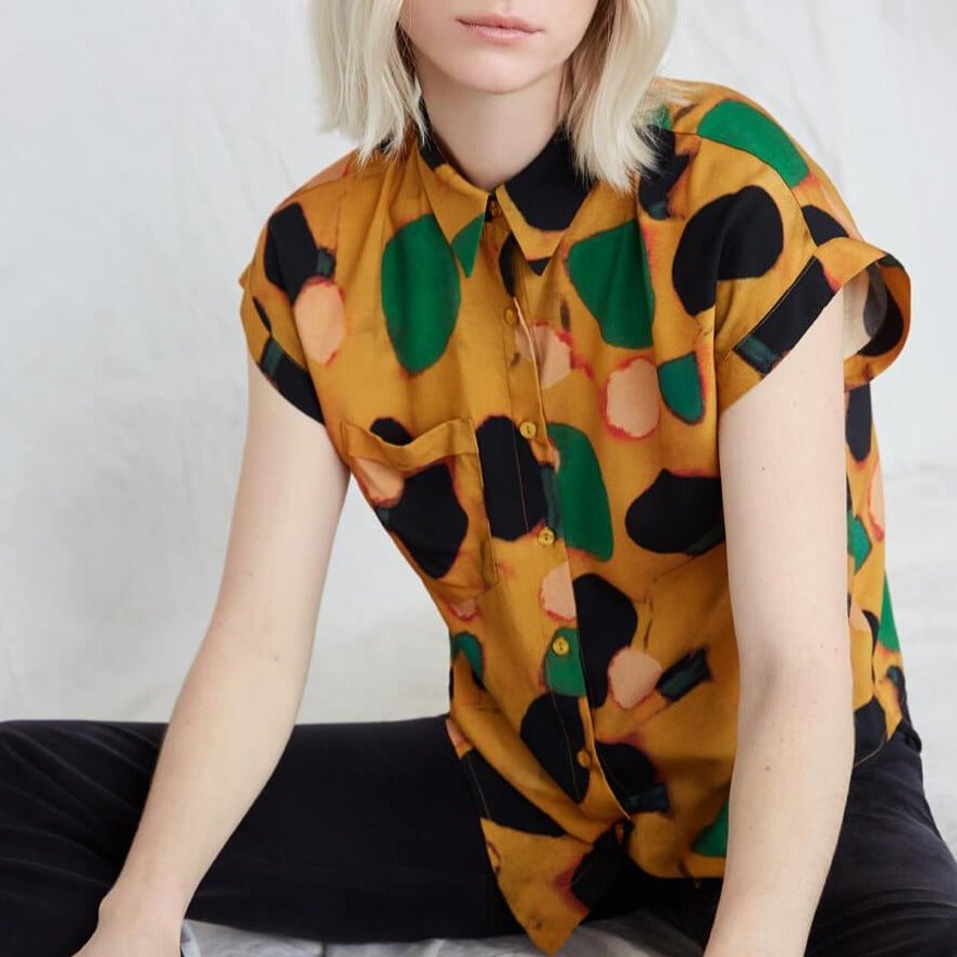 Blonde woman wears a boxy yellow button-down blouse with green, black and pink dots and black pants. The Caravan Shirt  in Klimt is from Canadian designer Eve Gravel. Illustrative pattern is a collaboration with artist Catherine D'Amours.