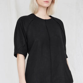 Blonde woman wears a slightly loose black dress with raglan sleeves. The Moonless Night Dress in Black features a sleek stitching detail down the front. The dress is from Canadian designer Eve Gravel.